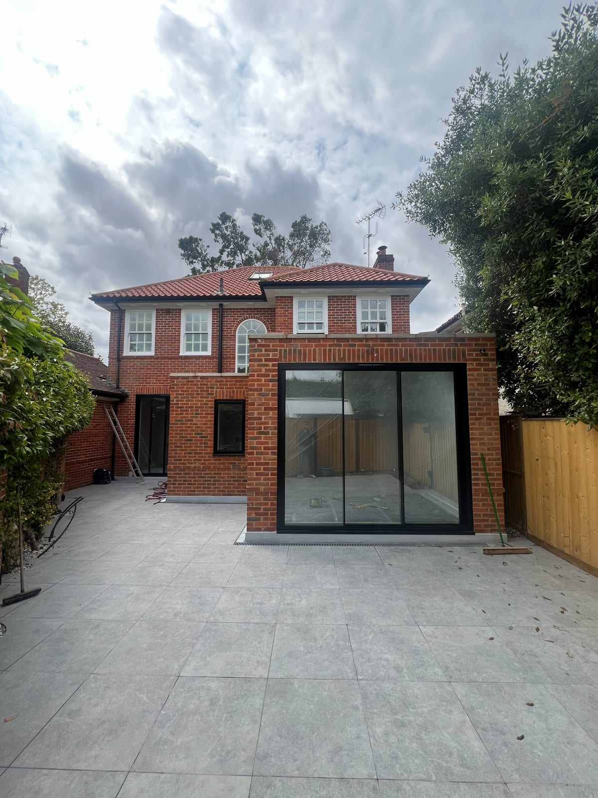 Completed single-storey brick rear extension with full-width black-framed sliding doors and a new patio, Richmond upon Thames
